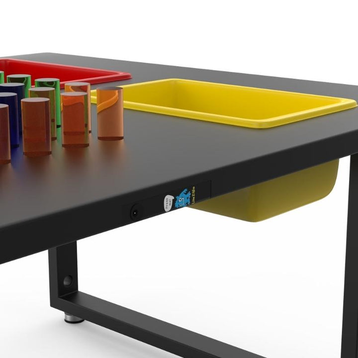 Close-up of the LiteZilla IllumiTable in Black HDPE finish showing the power button, Mini LitePins, and yellow storage bin on this LED sensory light table