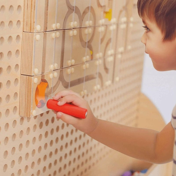 Close-up of a child's hands placing a component on the LiteZilla KidWorx bead maze wall panel, showing the tactile, hands-on interaction that supports sensory and fine motor development