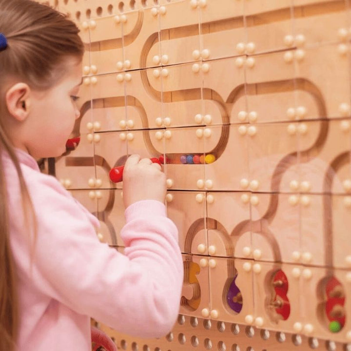 Child threading colourful beads through a curved bead maze panel on the LiteZilla KidWorx wall-mounted learning system, supporting fine motor development and cognitive sequencing