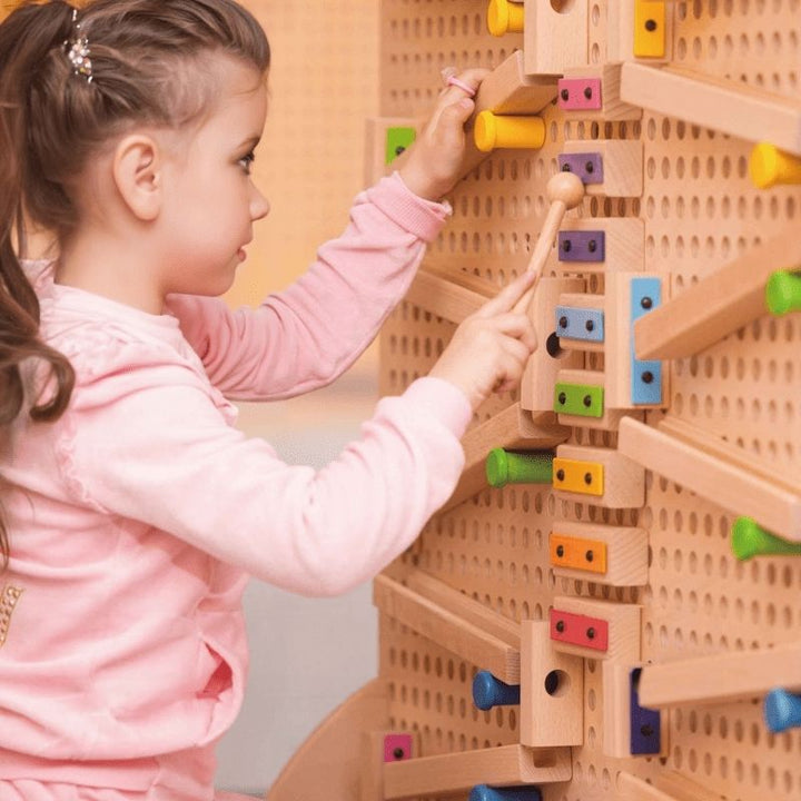 Child building a marble run pathway on the LiteZilla KidWorx modular wall system, using colourful connector pieces to develop hand-eye coordination and problem-solving skills