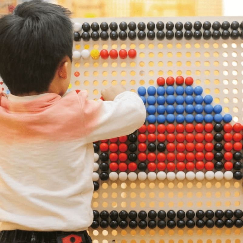Child creating a coloured car mosaic with dome-shaped pegs on the LiteZilla KidWorx interactive wall panel, an engaging STEM and creative play activity for schools and learning centres