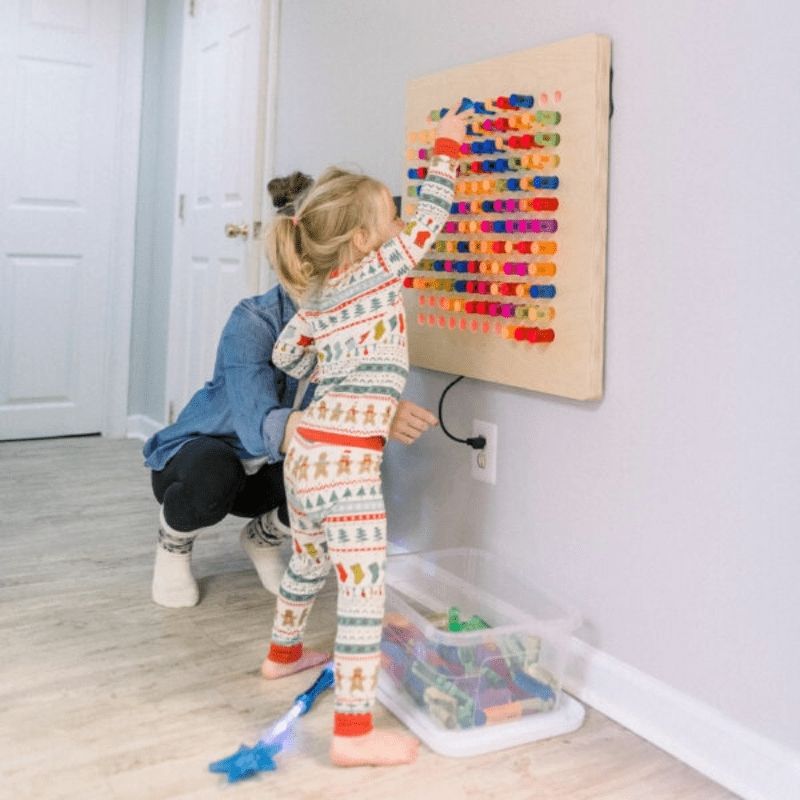 Two children engaging with the LiteZilla Mini tabletop lite brite mounted on a wall in a sensory room setting