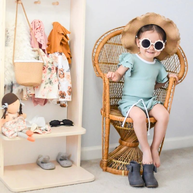 Child sitting on the Sapiens Child Mango Montessori Cubby Coat Rack seat, showing the correctly proportioned height for toddlers to sit independently while putting on or taking off shoes