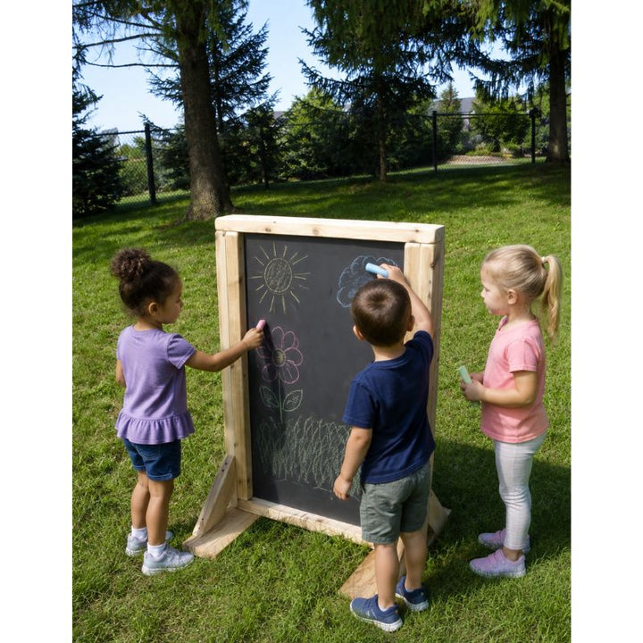 Three children drawing with chalk on the ONP Double Sided Art Easel outdoors, creating sun, flower and cloud designs on the chalkboard surface