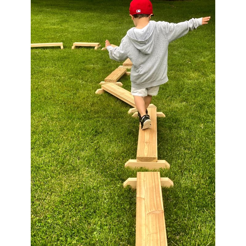 Child playing with the ONP Gross Motor Boards set of 8 Western Red Cedar balance boards, demonstrating an outdoor active play configuration using the variable-length cedar boards for gross motor development in early years settings across Canada and the US
