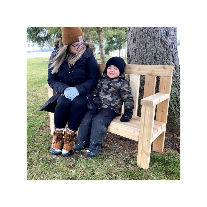 Mother and child sitting together on the ONP Infant Buddy Bench, demonstrating the 5-inch cedar seat height and taller armrests that support caregiver comfort at floor level in outdoor infant room and early years settings across Canada and the US