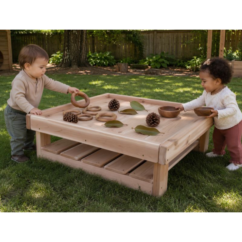 Two toddlers playing at the low ONP Infant Square Table outdoors, sorting wooden rings, bowls, pinecones and leaves on the tray surface