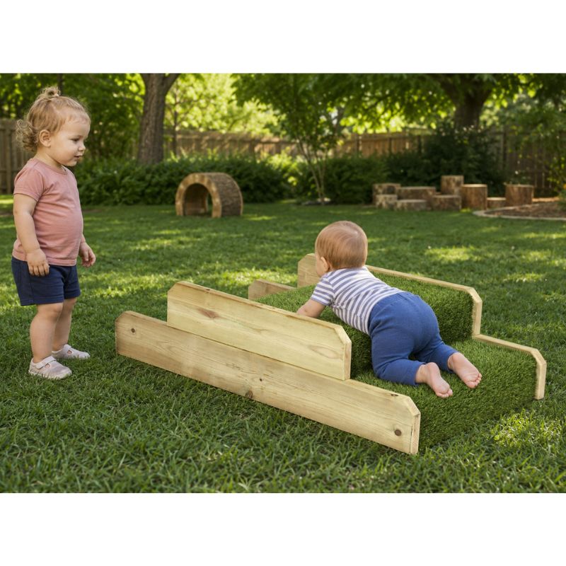 An infant crawling over the turf-covered ONP Infant Step and Ramp outdoors, with a toddler standing beside it