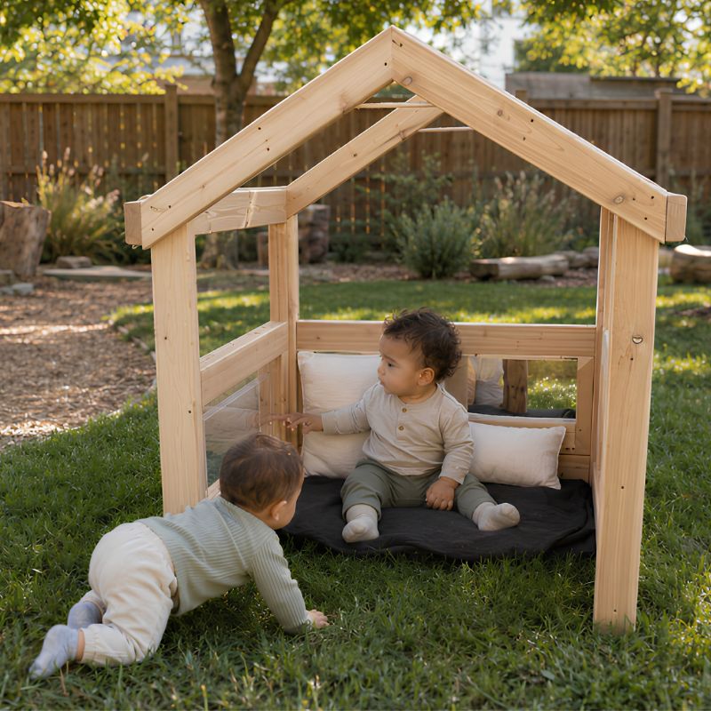 Two infants playing at the ONP Outdoor Baby Den outdoors, one crawling on grass and one seated inside on cushions