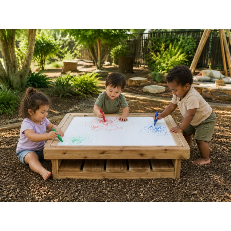 Three children drawing with crayons on the ONP Outdoor Square Art Table outdoors, using the whiteboard surface with a storage shelf below