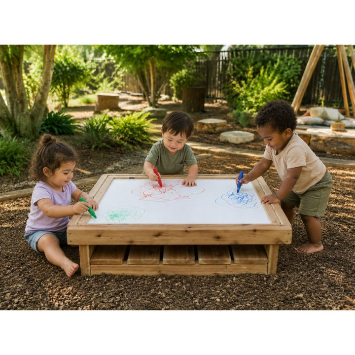 Three children drawing with crayons on the ONP Outdoor Square Art Table outdoors, using the whiteboard surface with a storage shelf below