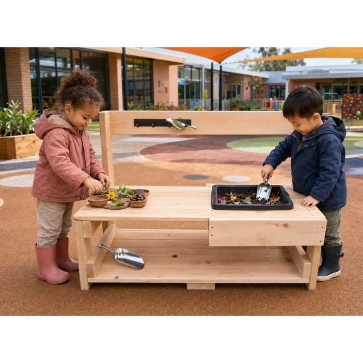 Two toddlers using the ONP Toddler Mud Kitchen outdoors, mixing petals and soil in the built-in tray with metal scoops
