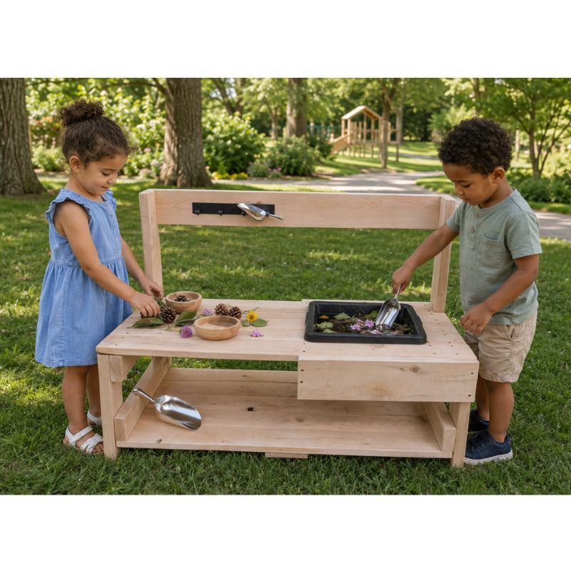 Two children playing at the ONP Toddler Mud Kitchen on grass, scooping soil and petals into the mixing tray