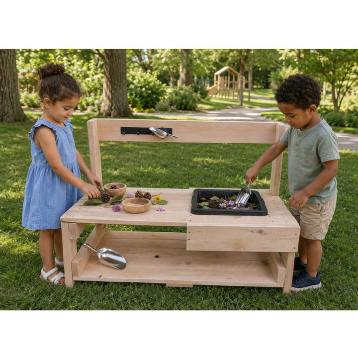 Two children playing at the ONP Toddler Mud Kitchen on grass, scooping soil and petals into the mixing tray