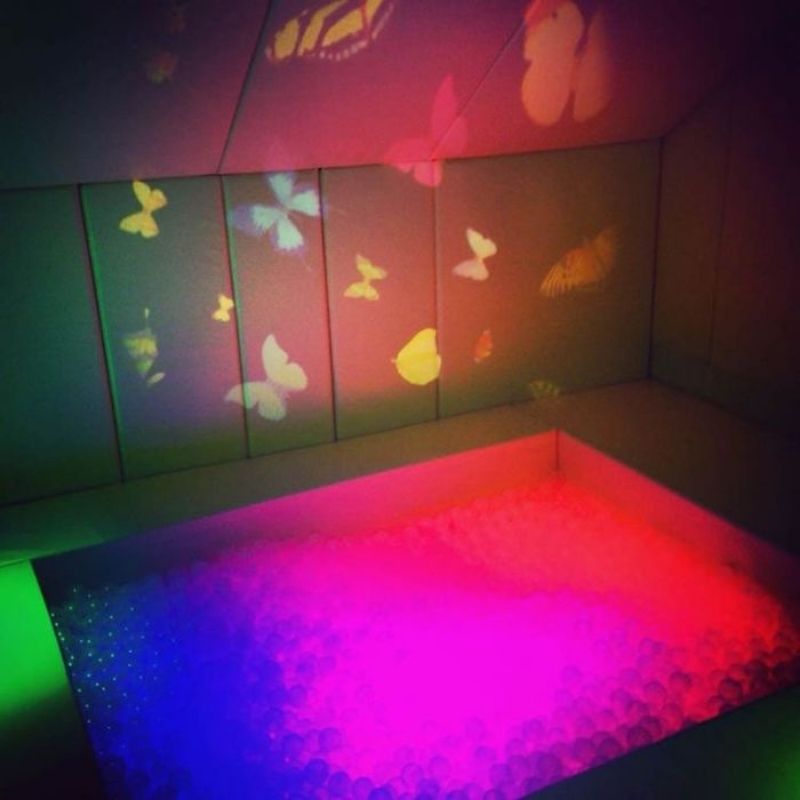 OPTIKinetics Solar 100 LED projector casting a butterfly effect wheel projection across a therapy room wall, creating a calming visual sensory environment