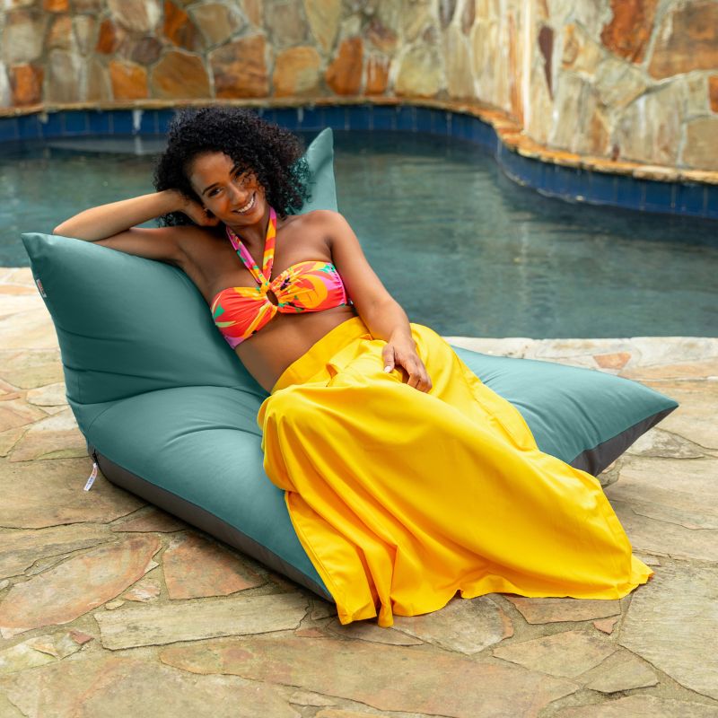 Woman lounging on the Jaxx Finster outdoor bean bag chair in Breeze Sunbrella fabric