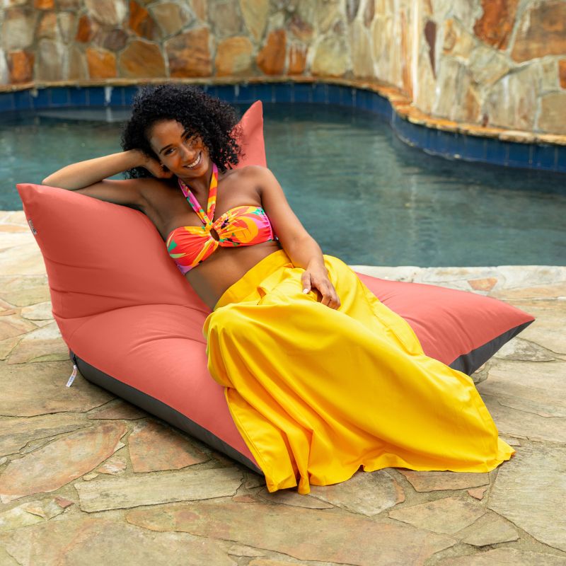 Woman lounging on the Jaxx Finster outdoor bean bag chair in flamingo Sunbrella fabric