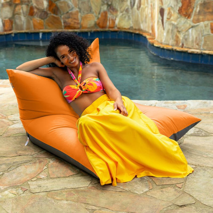Woman lounging on the Jaxx Finster outdoor bean bag chair in Tangerine Sunbrella fabric