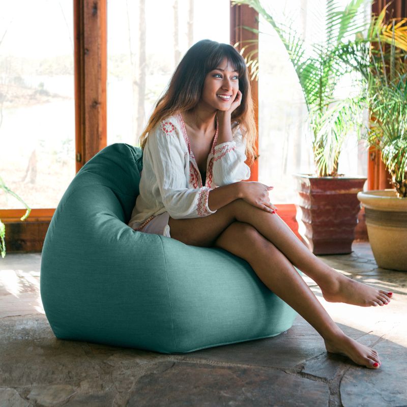 Woman relaxing in a Breeze Jaxx Kiss outdoor bean bag chair in a sunlit indoor space