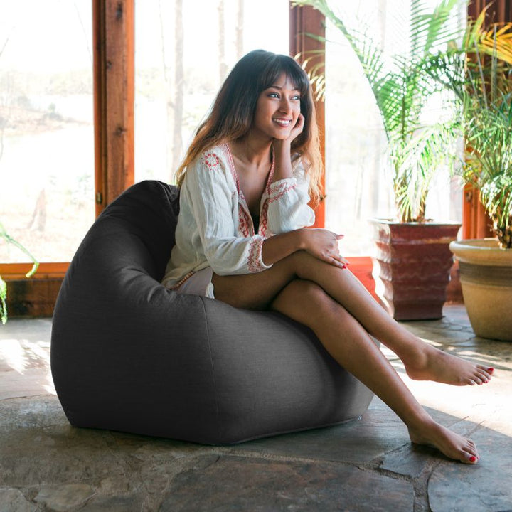Woman relaxing in a Charcoal Jaxx Kiss outdoor bean bag chair in a sunlit indoor space