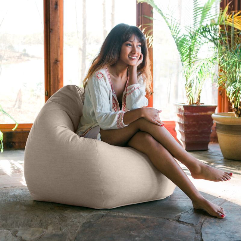 Woman relaxing in a Flax Jaxx Kiss outdoor bean bag chair in a sunlit indoor space