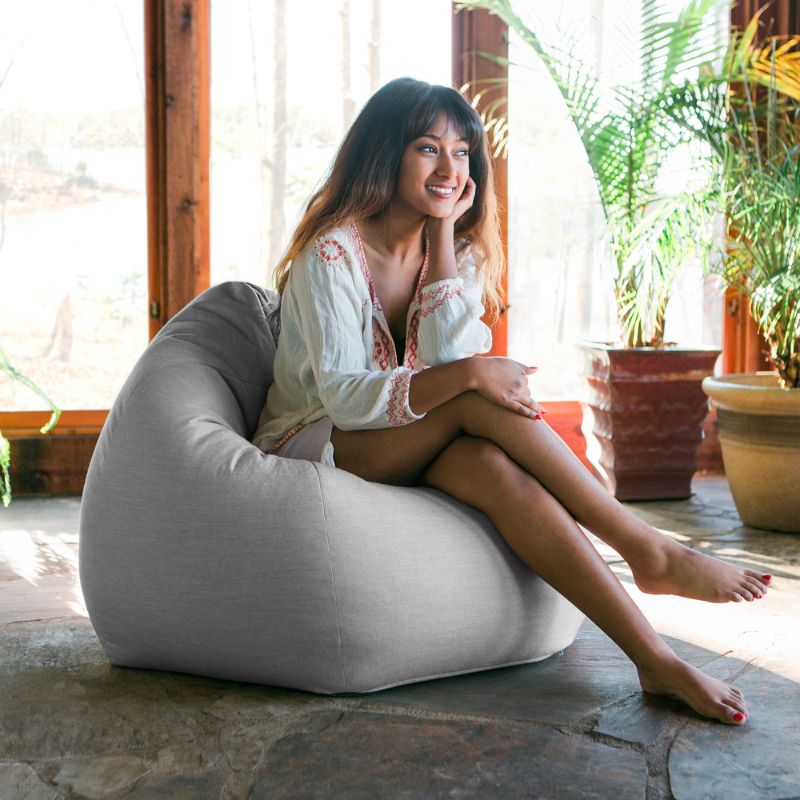 Woman relaxing in a Granite Jaxx Kiss outdoor bean bag chair in a sunlit indoor space