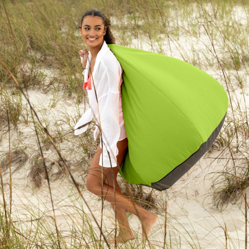 Woman carrying a Lime Jaxx Kiss outdoor bean bag chair across the beach dunes