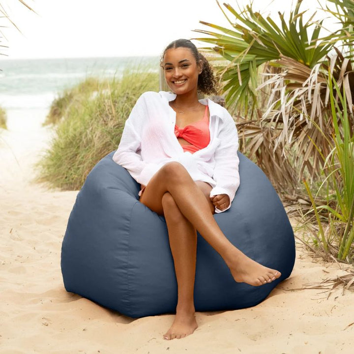 Woman relaxing in a Navy Jaxx Kiss outdoor bean bag chair near beach dunes