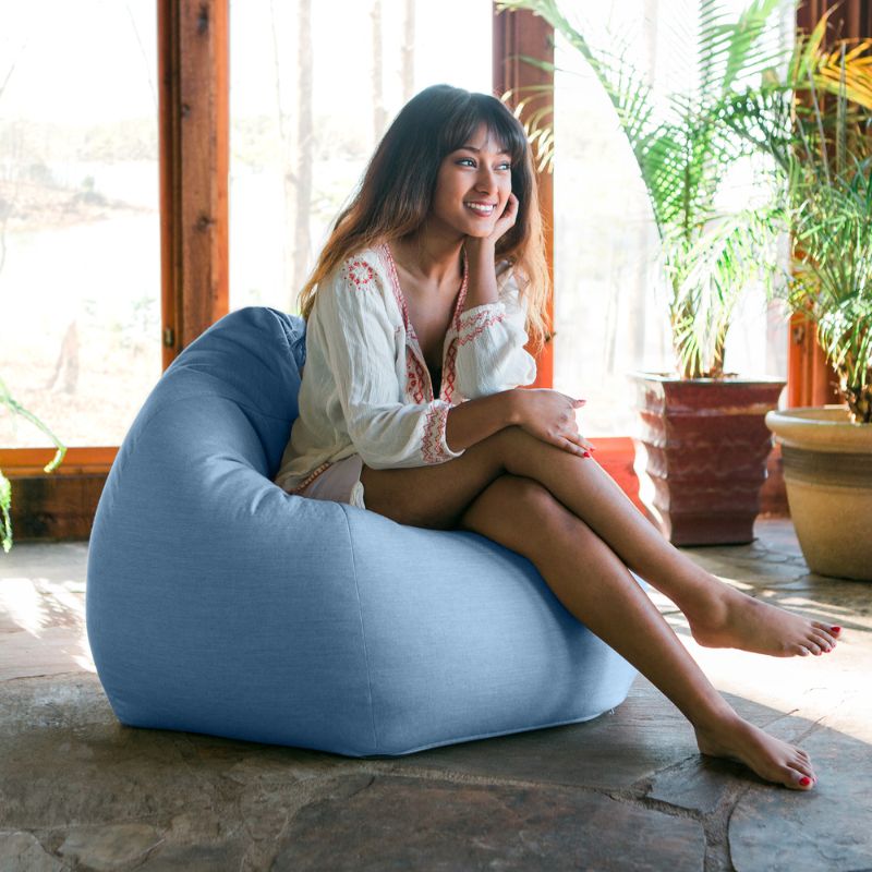 Woman relaxing in an Ocean Blue Jaxx Kiss outdoor bean bag chair in a sunlit indoor space