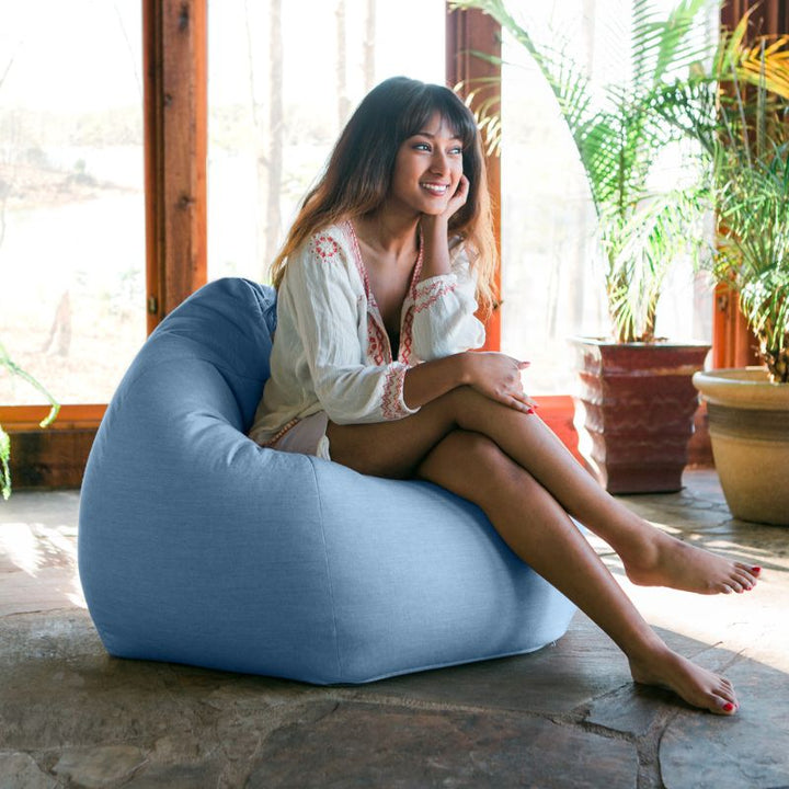 Woman relaxing in an Ocean Blue Jaxx Kiss outdoor bean bag chair in a sunlit indoor space