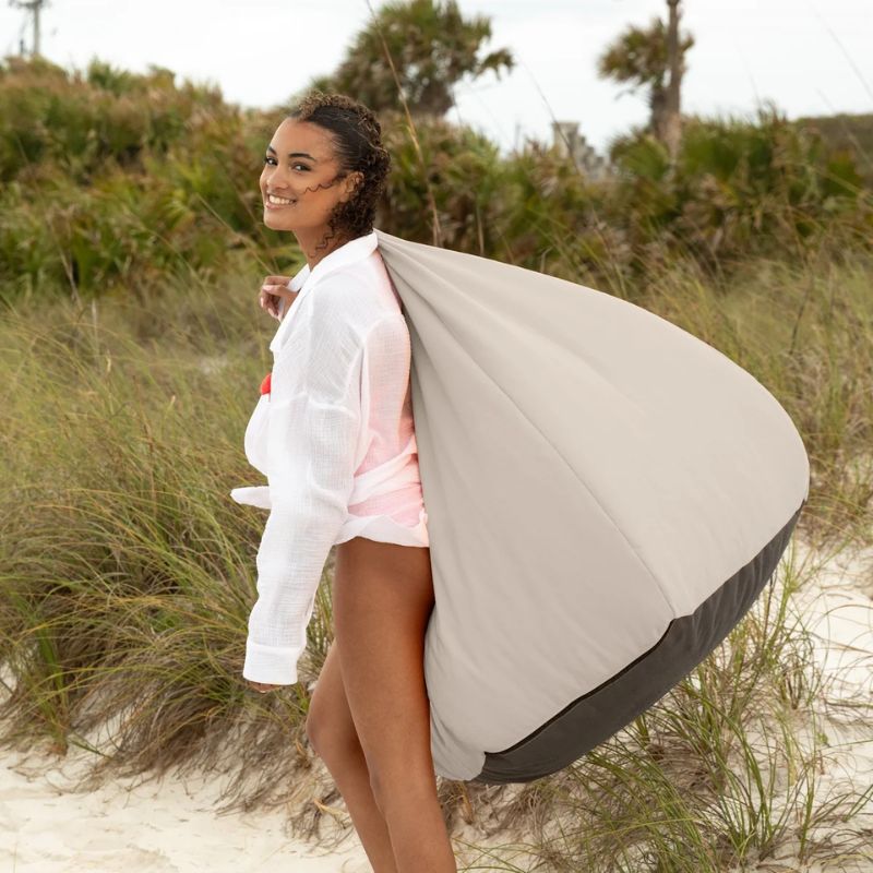 Woman carrying a Pearl Jaxx Kiss outdoor bean bag chair by its handle on the beach