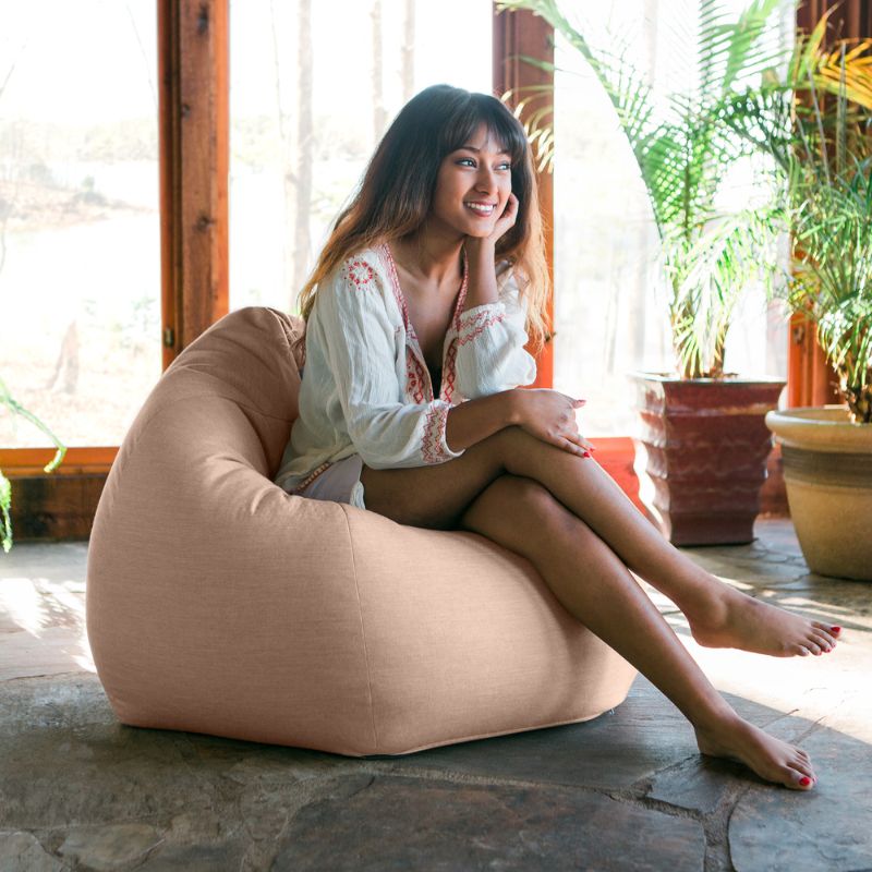 Woman relaxing in a Petal Jaxx Kiss outdoor bean bag chair in a sunlit indoor space