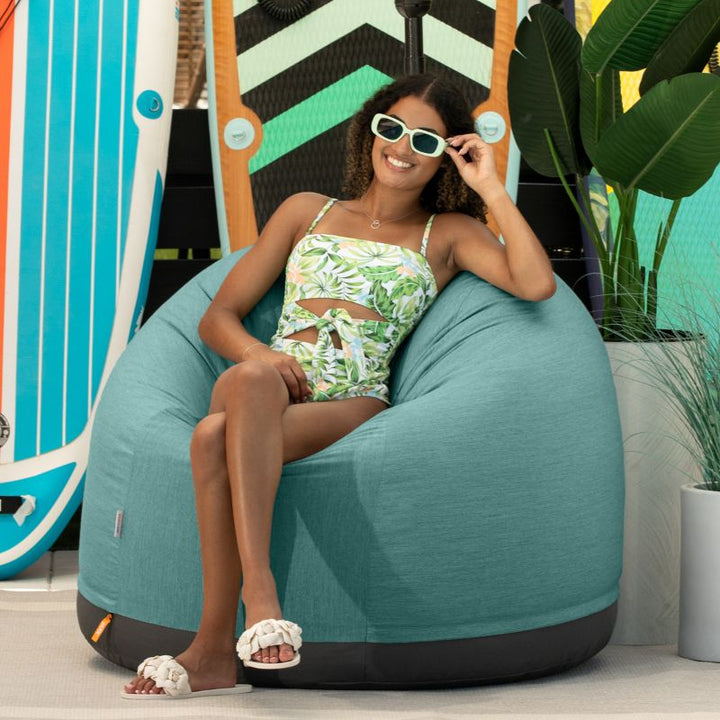 Woman relaxing on a beach in the Jaxx Palmetto outdoor bean bag chair in Breeze Sunbrella fabric