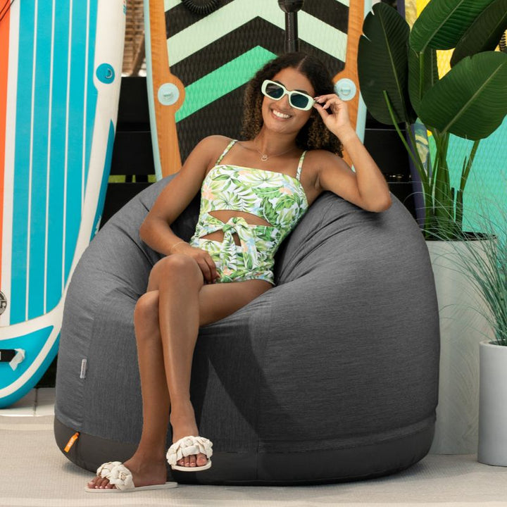 Woman seated outdoors in the Jaxx Palmetto weatherproof bean bag chair in Charcoal Sunbrella fabric