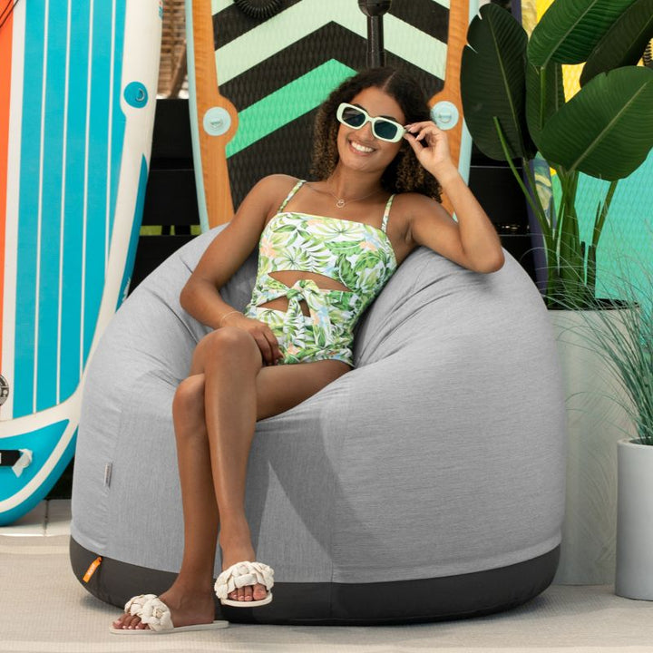 Woman relaxing on a beach in the Jaxx Palmetto outdoor bean bag chair in Granite Sunbrella fabric