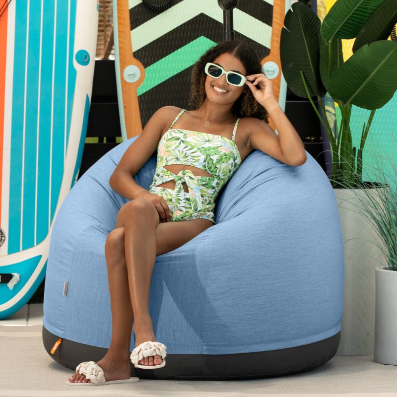 Woman relaxing on a beach in the Jaxx Palmetto outdoor bean bag chair in Ocean Blue Sunbrella fabric