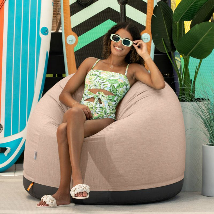 Woman relaxing on a beach in the Jaxx Palmetto outdoor bean bag chair in Petal Sunbrella fabric
