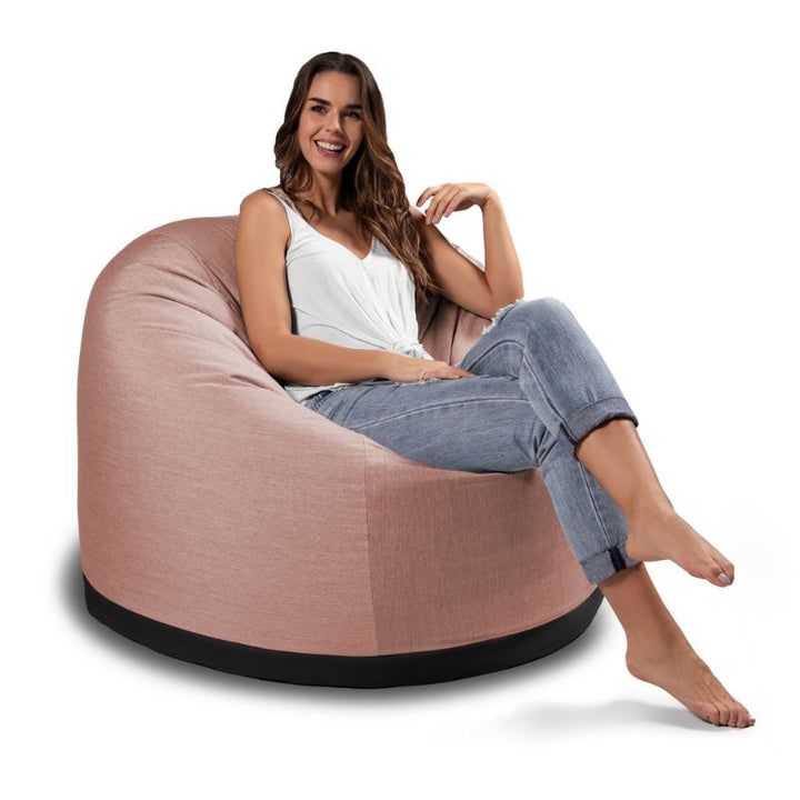 Woman sitting in the Jaxx Palmetto outdoor bean bag chair in Petal Sunbrella fabric