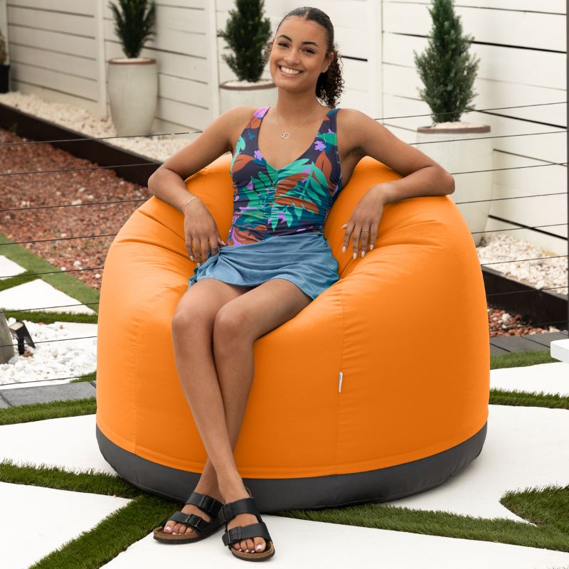Woman relaxing on a beach in the Jaxx Palmetto outdoor bean bag chair in Tangerine Sunbrella fabric