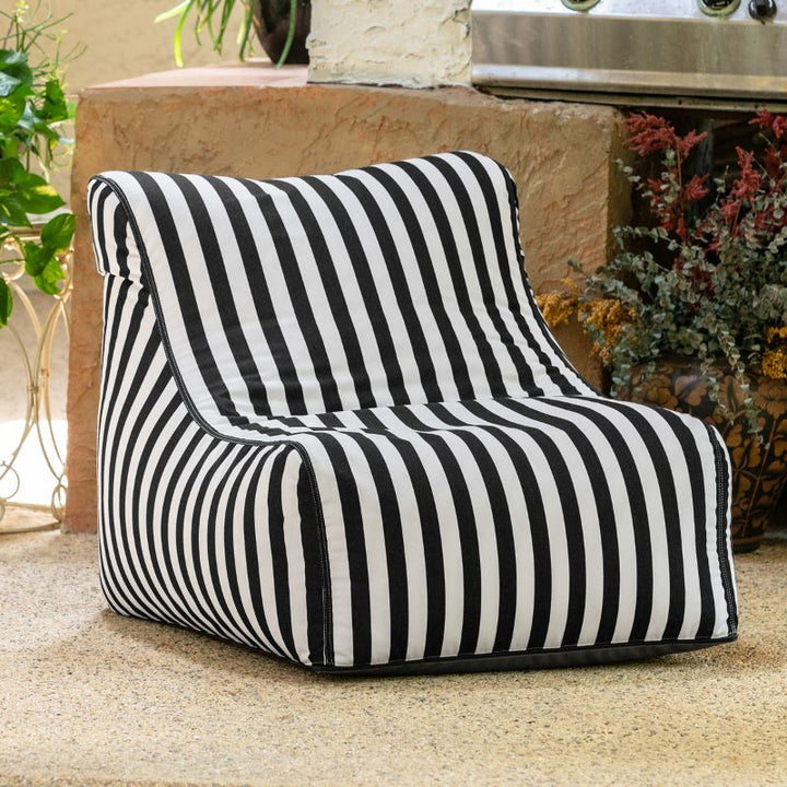 Jaxx Ponce Outdoor Bean Bag Chair in Black & White Stripes on a patio beside potted plants, a striped poolside bean bag for cozy outdoor corners
