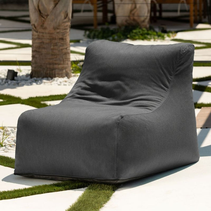 Jaxx Ponce Outdoor Bean Bag Chair in Charcoal in a sunny palm courtyard, a dark grey weather-resistant patio seat
