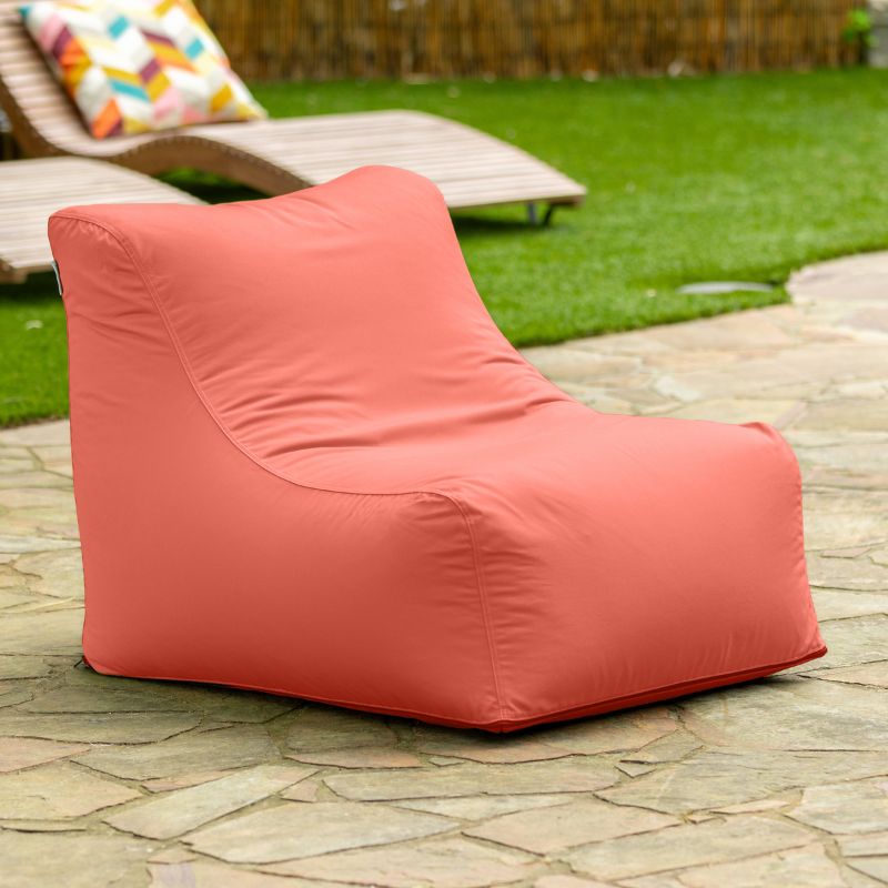 Jaxx Ponce Outdoor Bean Bag Chair in Flamingo on a flagstone patio beside a lounger, a coral poolside bean bag