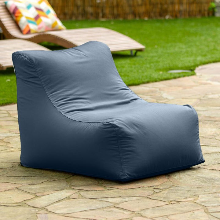 Jaxx Ponce Outdoor Bean Bag Chair in Navy on a stone patio near the lawn, a deep blue portable outdoor seat