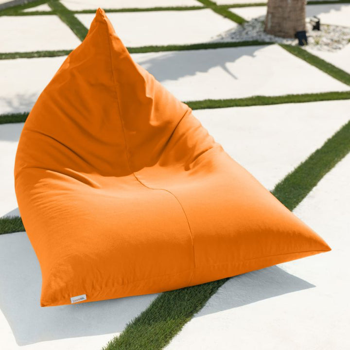 Bright orange Jaxx Twist Outdoor Bean Bag Chair in Sunbrella Tangerine on a turf-lined patio, a bold Sunbrella bean bag that keeps its color in the sun