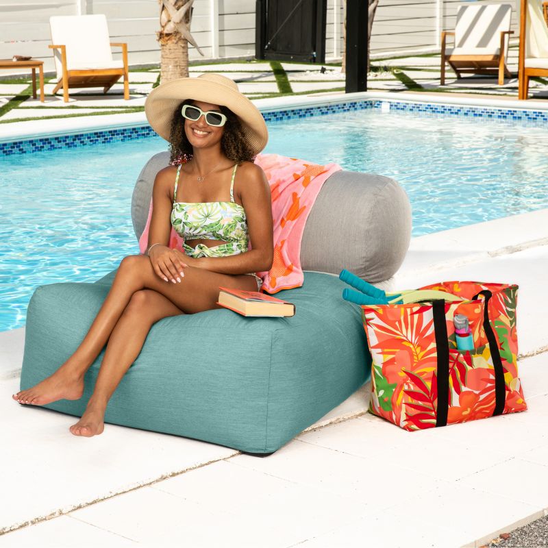 Woman relaxing by the pool on the Jaxx Tybee outdoor bean bag chair in Breeze Sunbrella, with a book resting on the seat