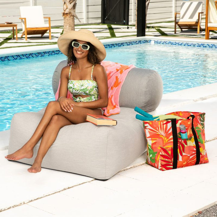 Woman sitting on the Jaxx Tybee outdoor bean bag chair in Flax Sunbrella, a low-profile patio bean bag chair beside the pool