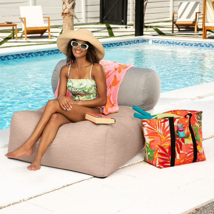 Woman lounging on the Jaxx Tybee outdoor bean bag chair in Petal Sunbrella, a soft outdoor seat for calm, sunny afternoons