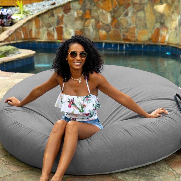 Woman relaxing poolside on the Jaxx Cocoon Outdoor bean bag in Charcoal fabric, weatherproof outdoor seating