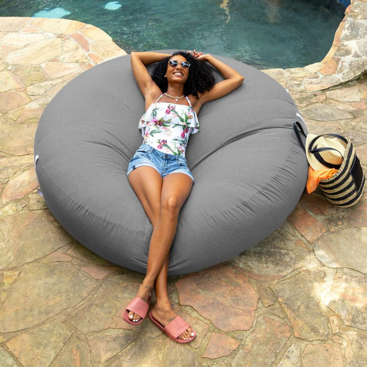 Woman relaxing poolside on the Jaxx Cocoon Outdoor bean bag in Charcoal fabric, weatherproof outdoor seating