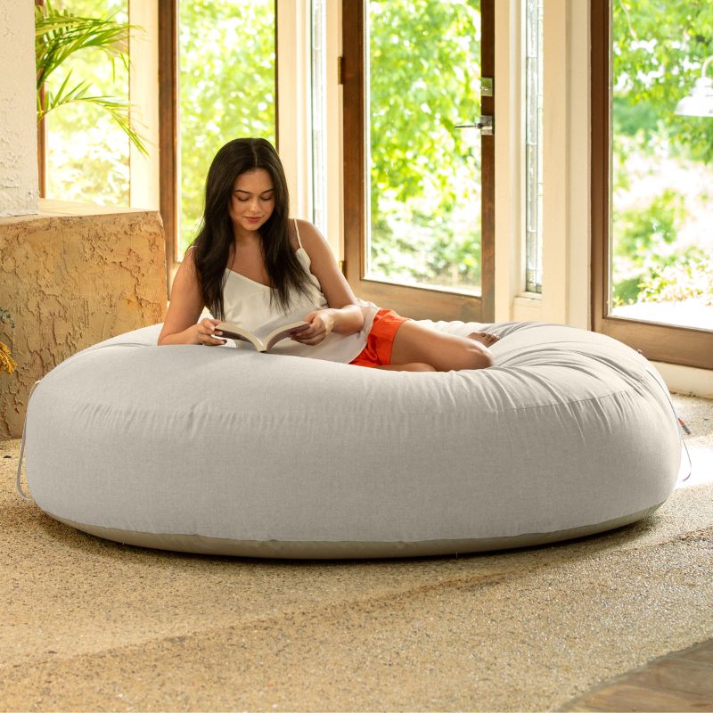 Woman reading on the Jaxx Cocoon Outdoor bean bag in Flax fabric, oversized deep pressure seating indoors